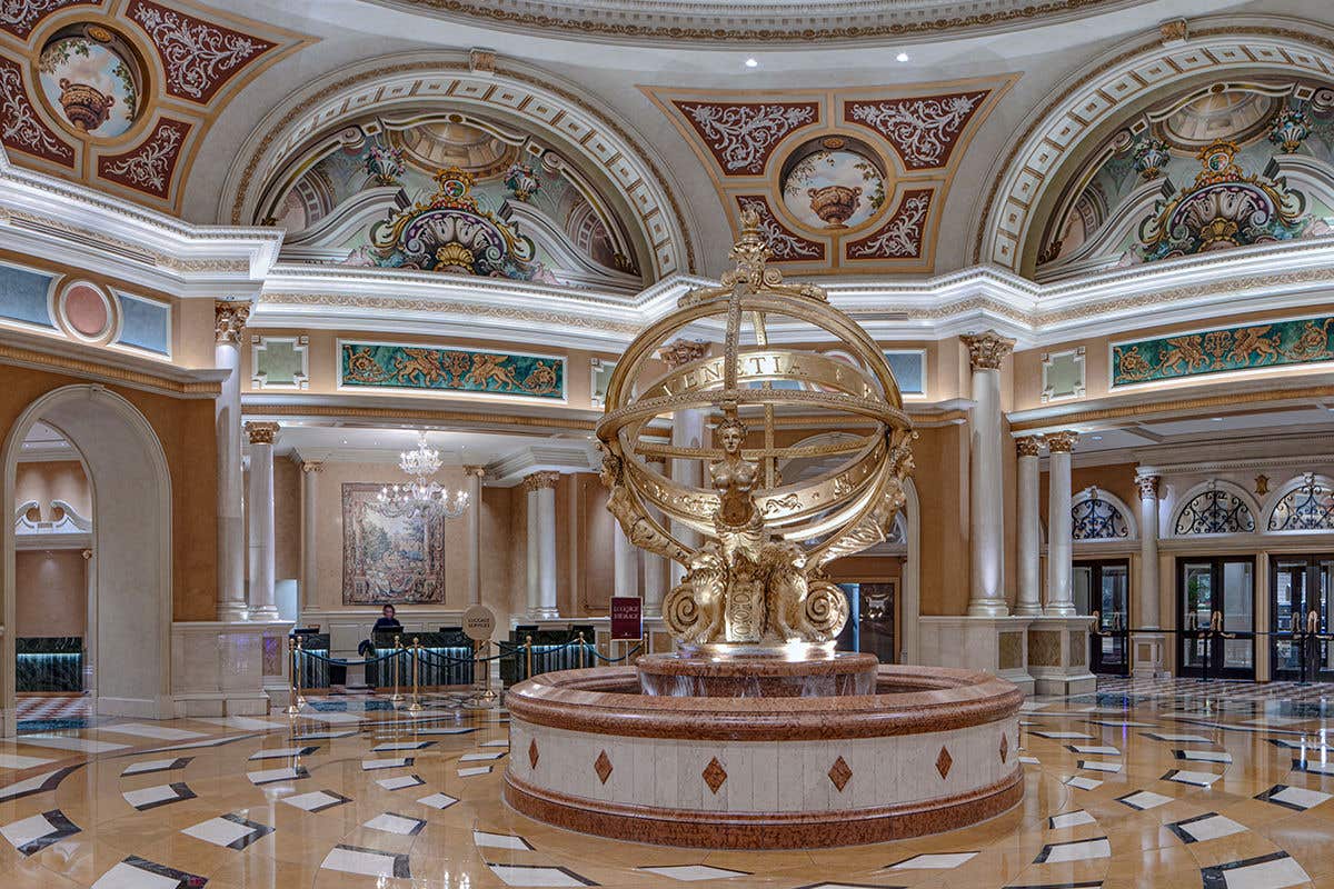 Opulent indoor fountain with a golden armillary sphere in a lavishly decorated lobby with marble floors and arched entries.