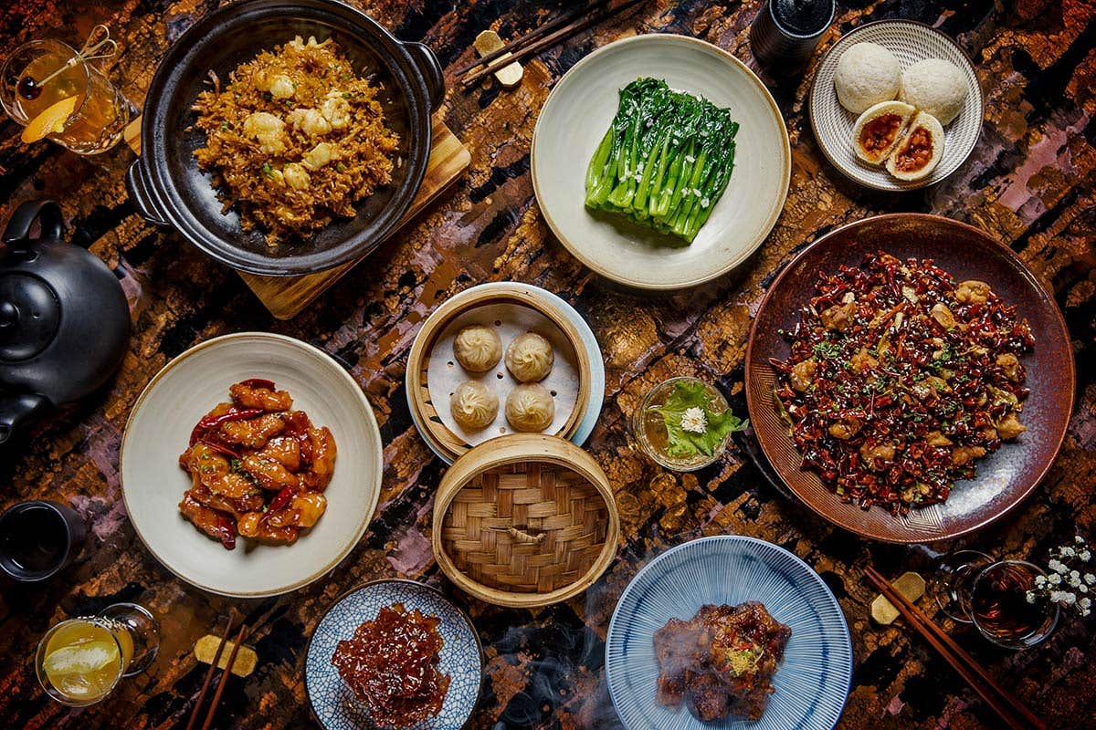 An assortment of Asian foods plated amongst chopsticks and cocktails. 